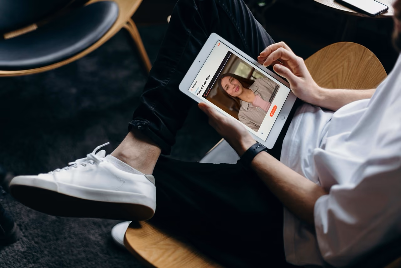 Person seated on chair watching a video of a woman on a tablet titled Price & Objections.