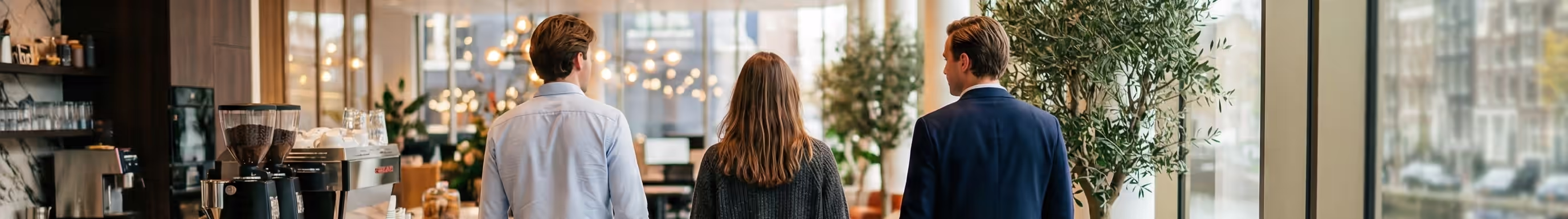 Three men sitting at a conference table with laptops, one drinking from a cup.