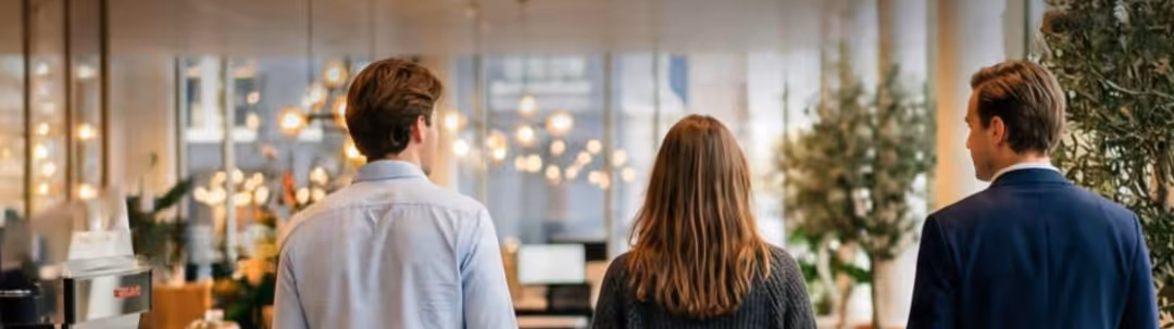 Three men sitting at a conference table with laptops, one drinking from a cup.