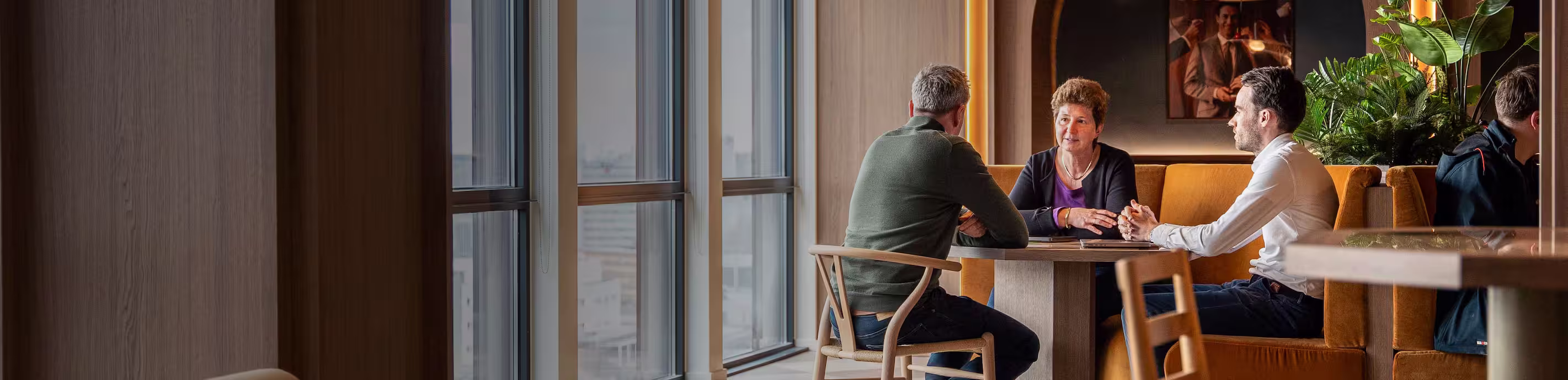 Two business professionals sitting on wooden steps in a modern office, engaged in conversation with one holding a tablet.