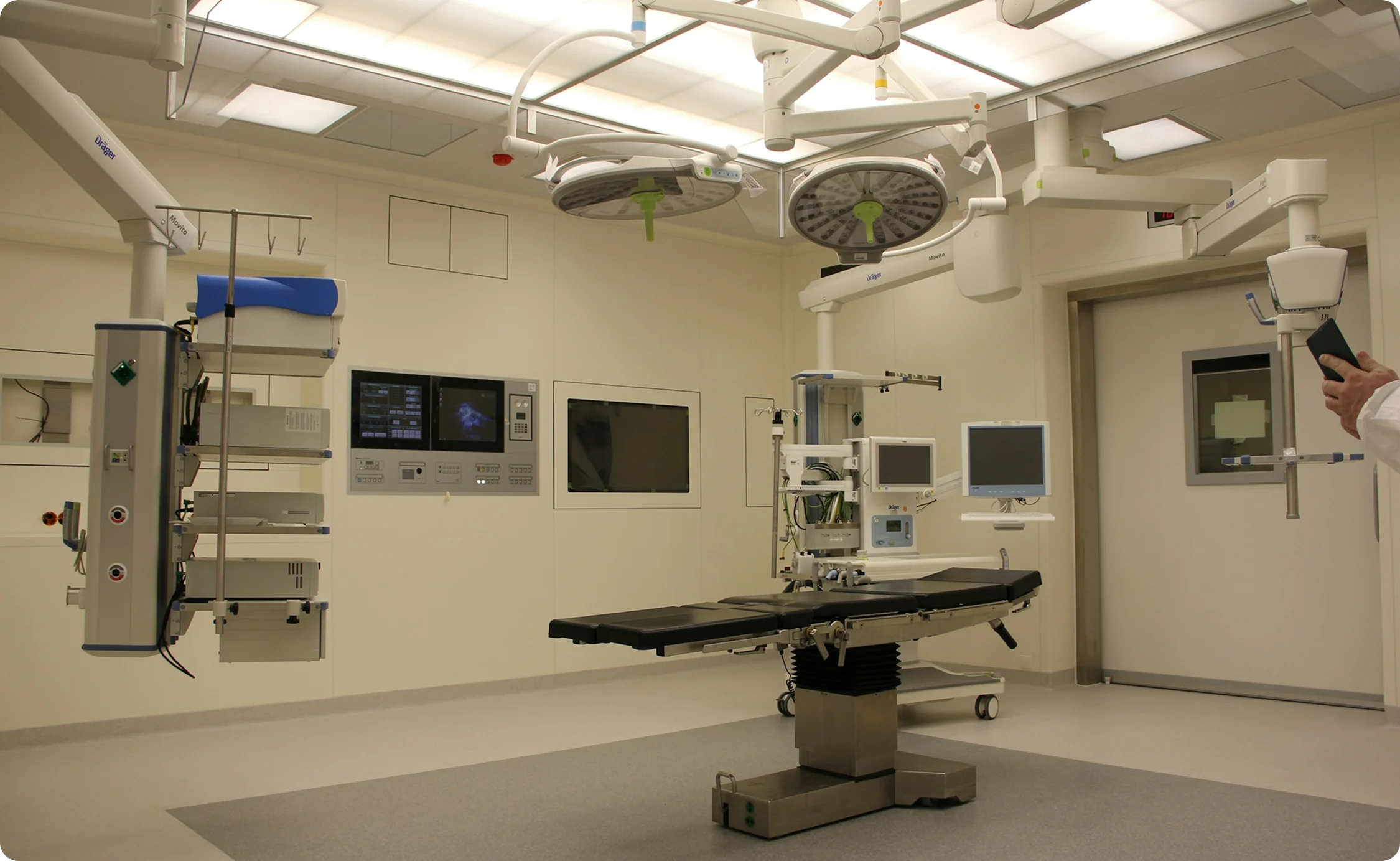 Modern, sterile operating room with surgical table, overhead surgical lights, medical monitors, and equipment.