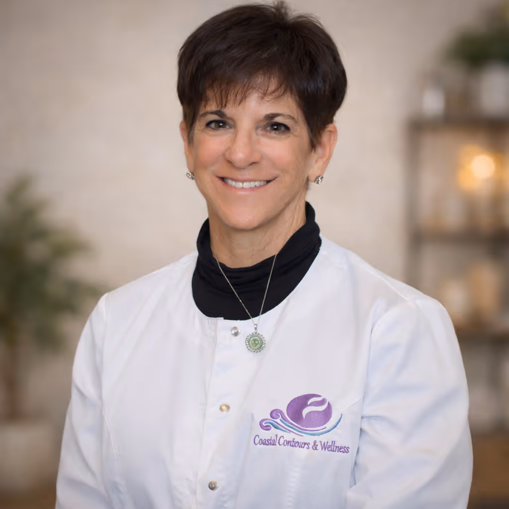 Smiling woman with short dark hair wearing a white coat with Coastal Contours & Wellness logo.