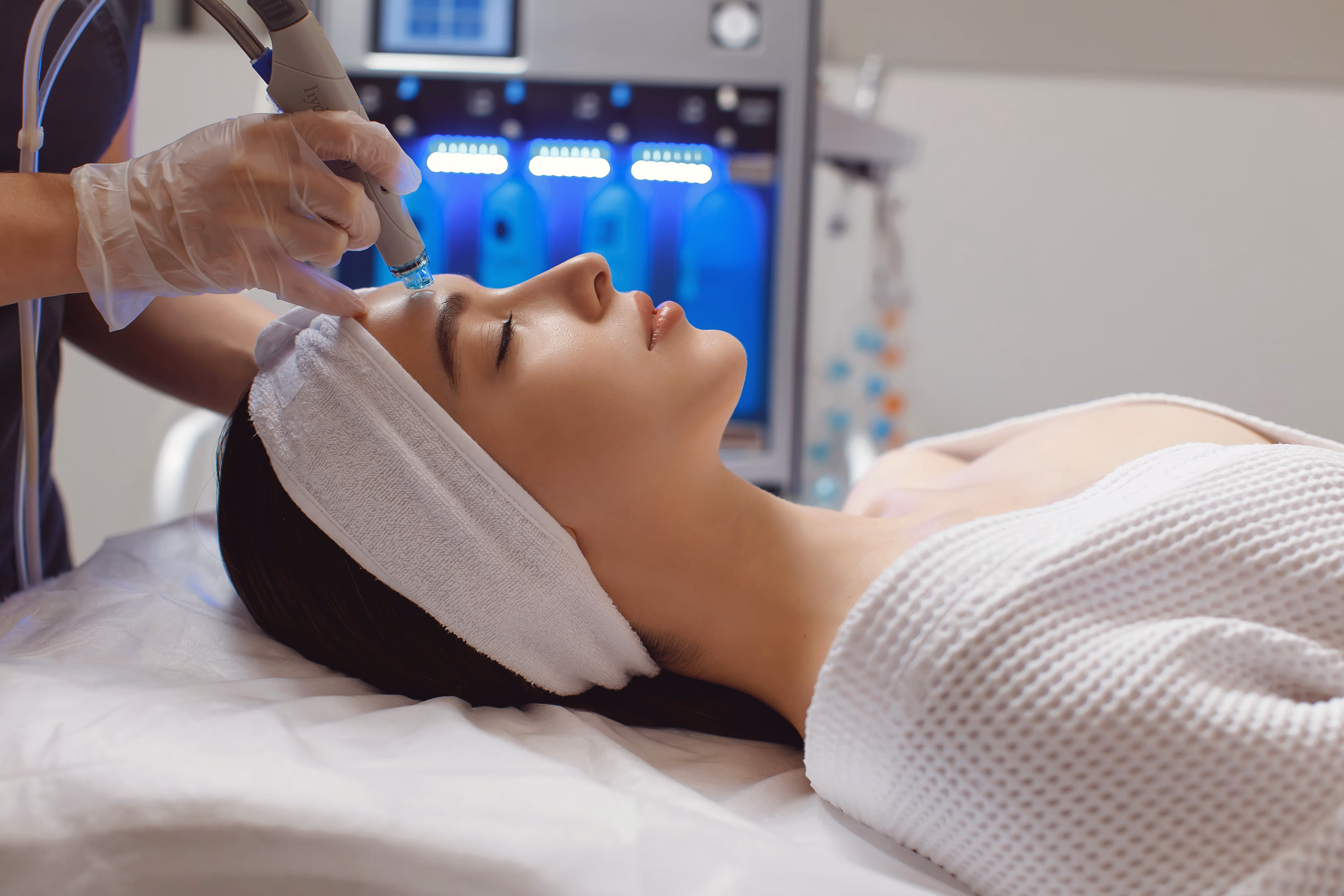 Woman receiving facial treatment with a blue light therapy device at a spa.