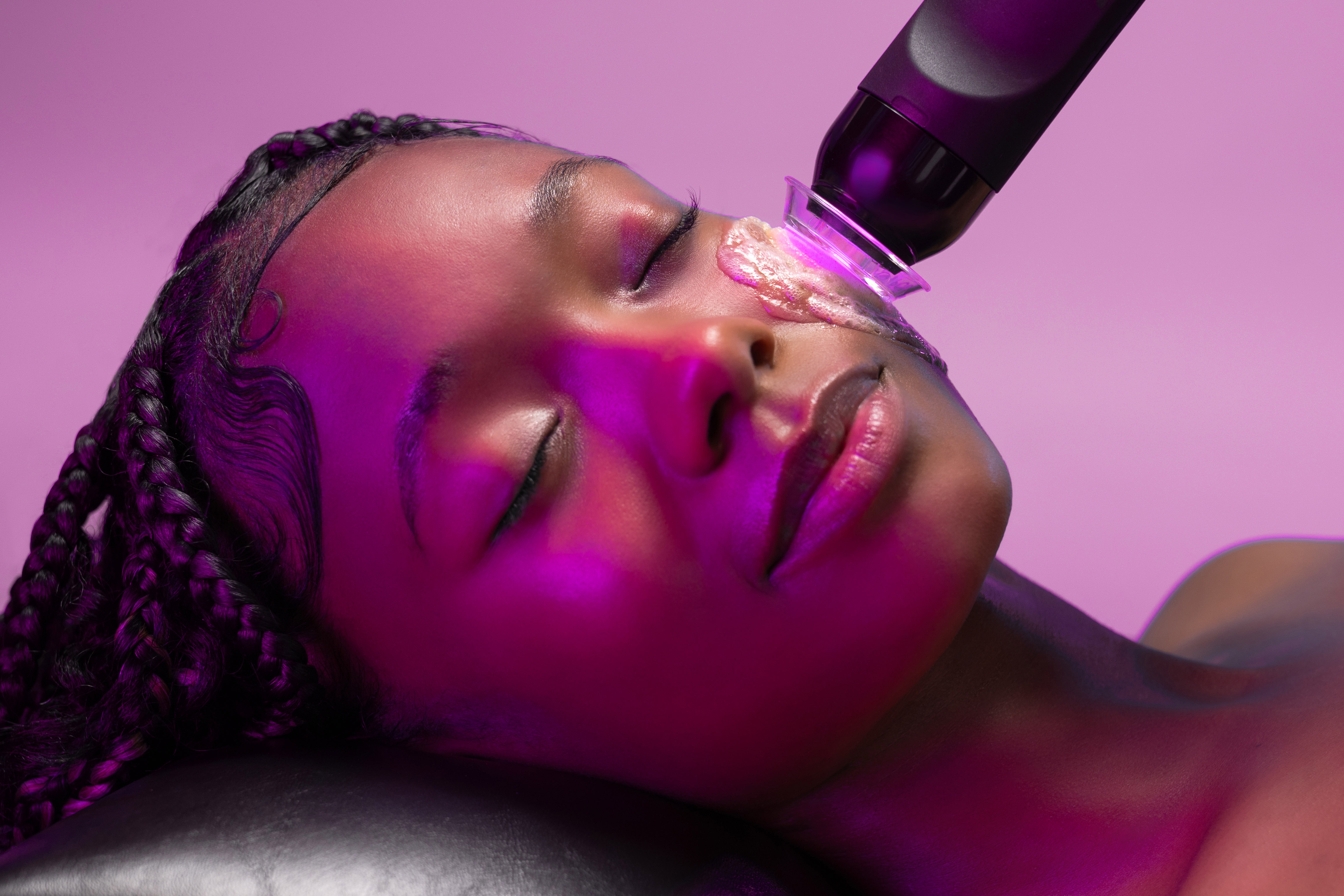 Woman receiving facial treatment with a blue light therapy device at a spa.
