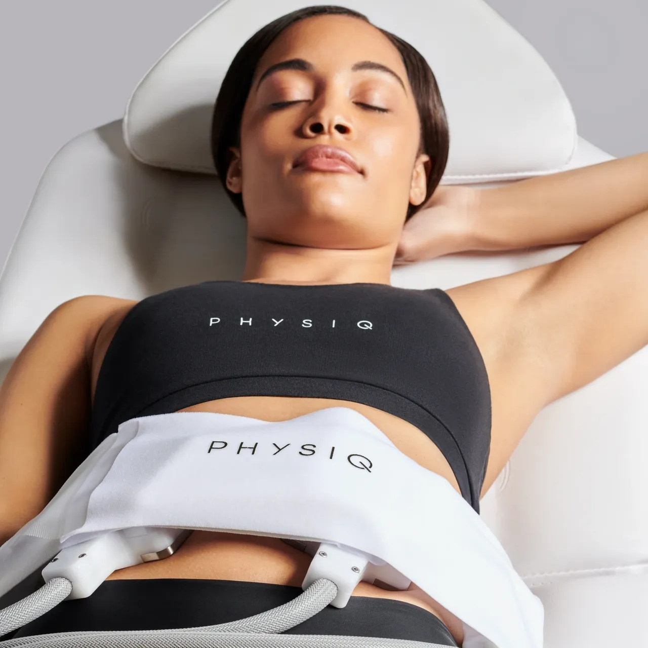 Woman lying on a treatment bed with a PHYSIQ device wrapped around her abdomen.