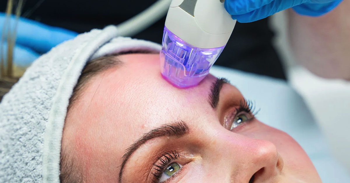 Woman receiving facial treatment with a blue light therapy device at a spa.