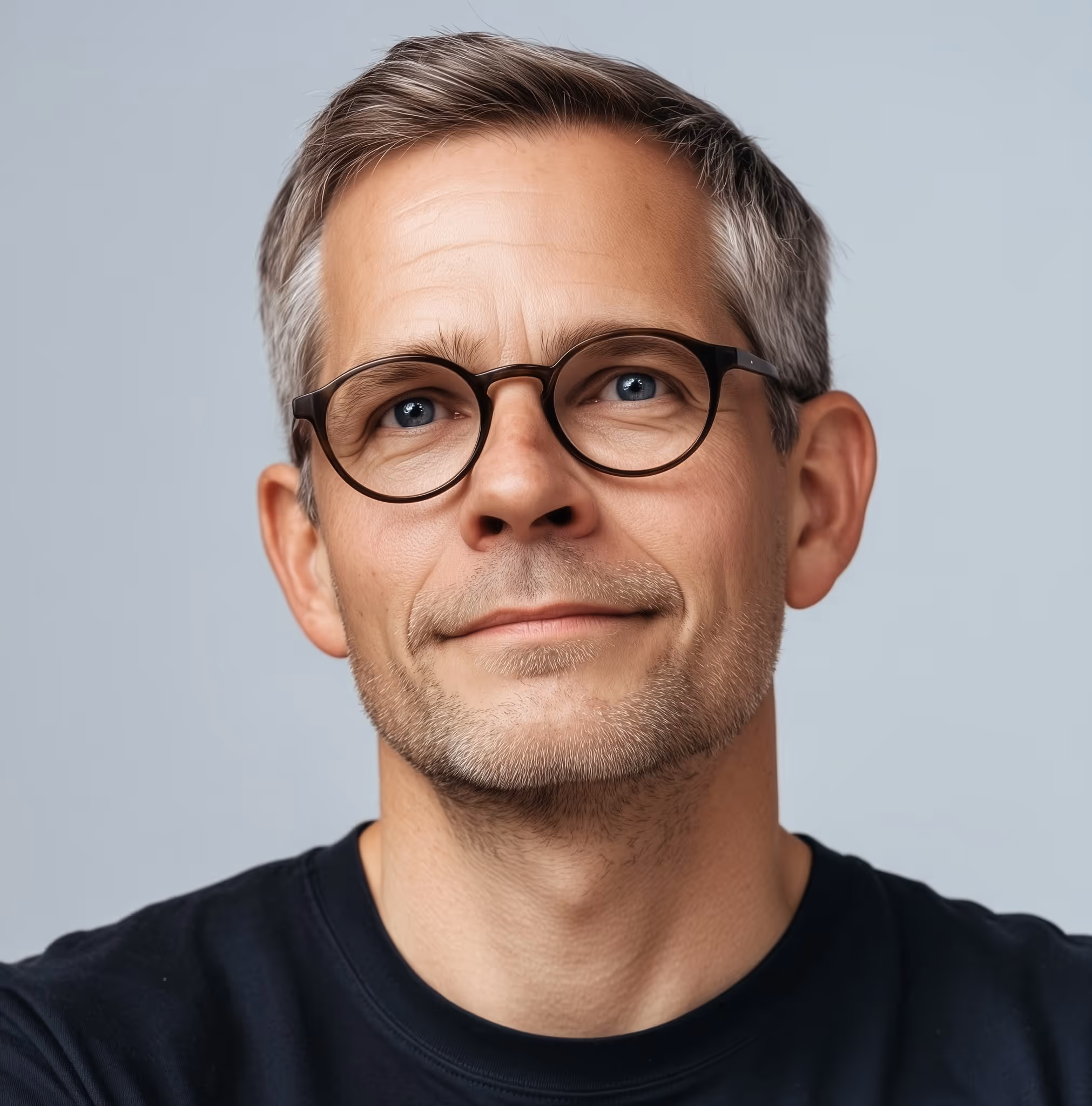 Portrait of a middle-aged man with short gray hair, blue eyes, glasses, and a slight smile wearing a black shirt.