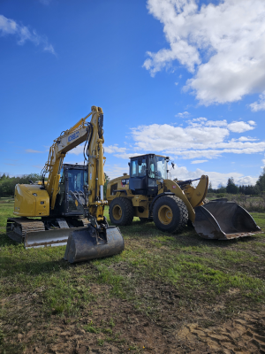 Two yellow excavators parked on grass under a partly cloudy blue sky.