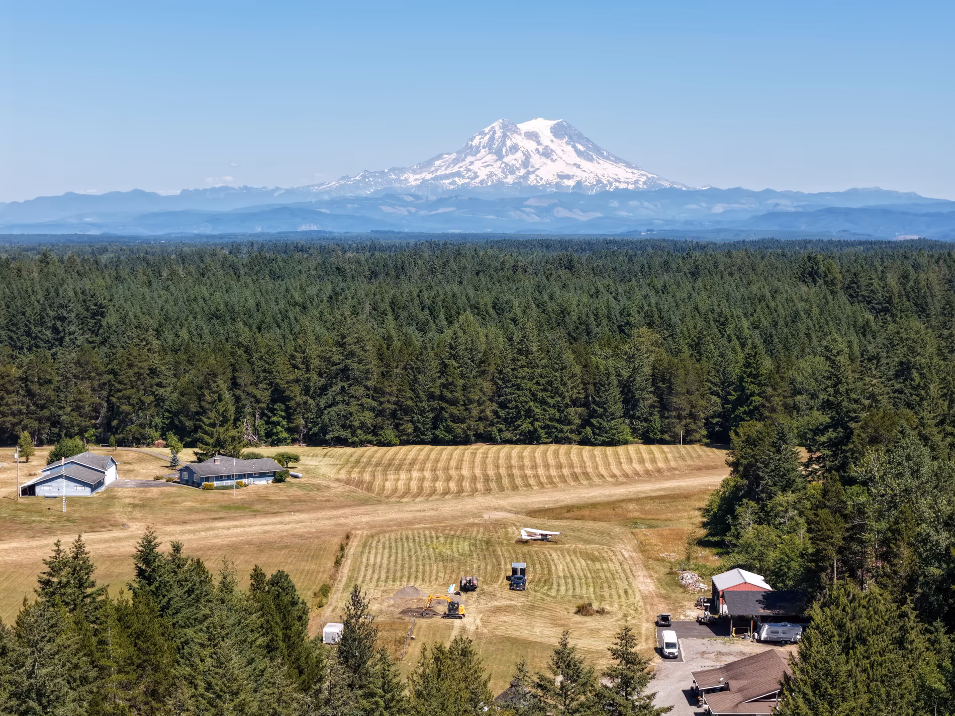 Mt. Rainier rises behind dense forest with worksite in the foreground.