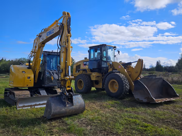 Two yellow excavators parked on grass under a partly cloudy blue sky.