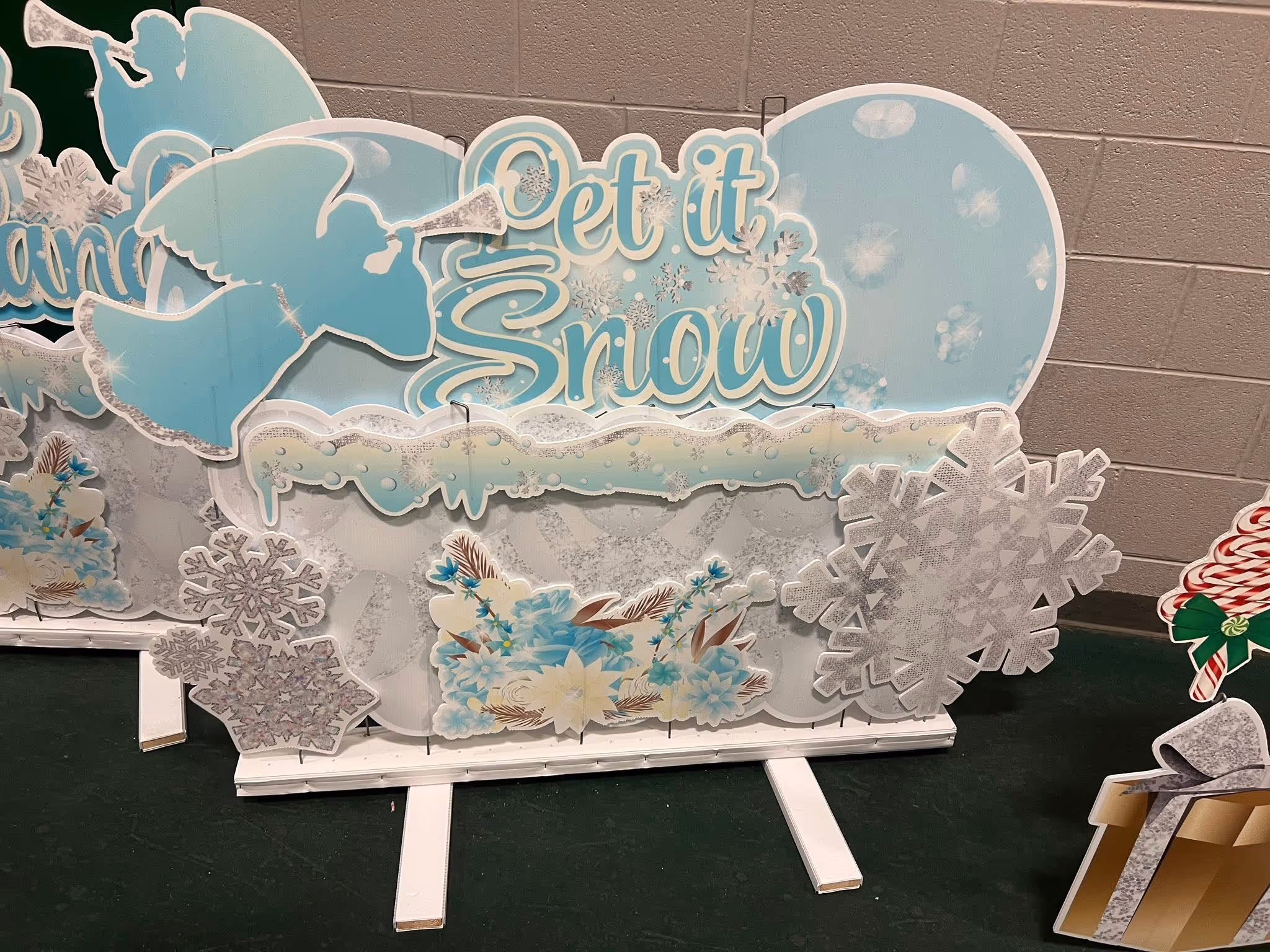 Decorative winter display with blue angels blowing trumpets, snowflakes, flowers, and the phrase 'Let it Snow.'