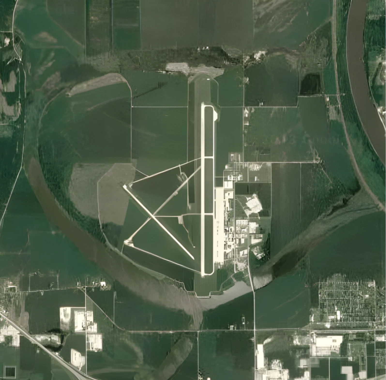 Aerial view of an airport with a single runway, taxiways, buildings, and surrounding farmland, bordered partially by a river.