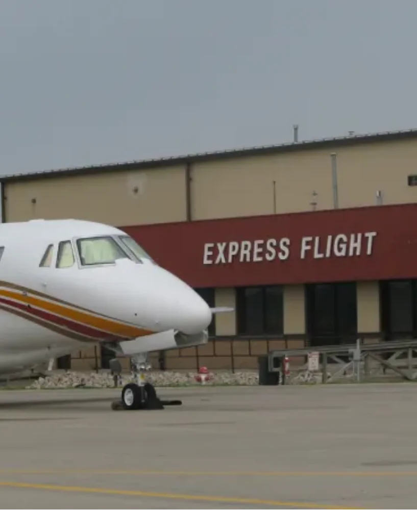 Front view of a white private jet parked on tarmac in front of a building with a sign reading 'EXPRESS FLIGHT'.