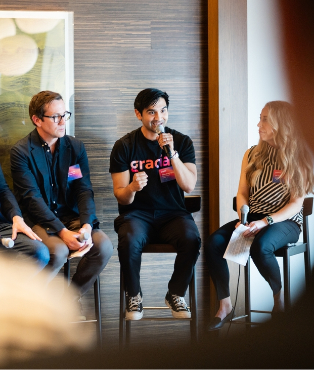 Three people sitting on stools during a panel discussion; the man in the center speaks into a microphone while the others listen.