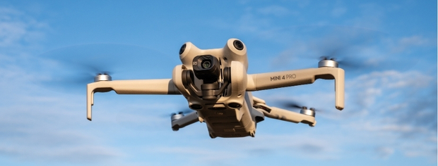 DJI Mini 4 Pro drone flying against a blue sky.