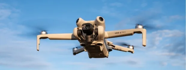 DJI Mini 4 Pro drone flying against a blue sky.