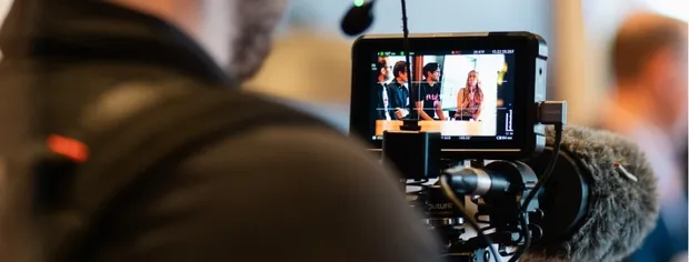 Close-up of a professional video camera's monitor showing three people in a discussion during a multi-camera recording.