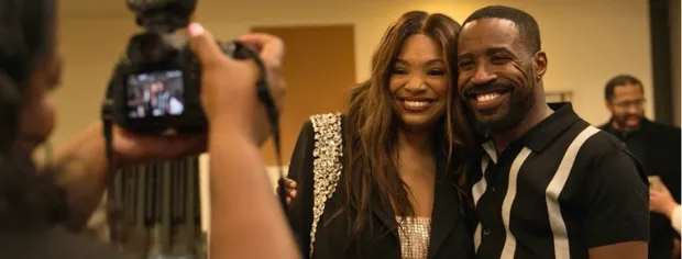 Smiling couple posing together as a photographer takes their picture indoors.