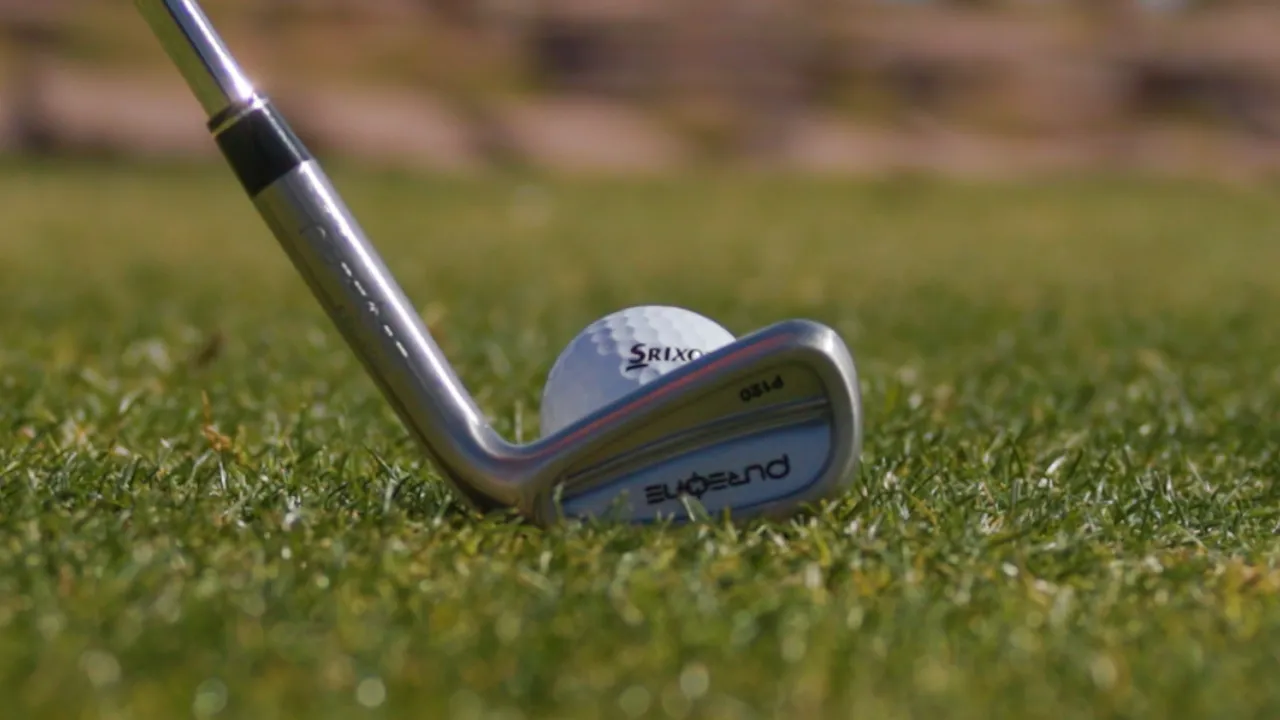 Close-up of a golf club positioned next to a golf ball on grass.