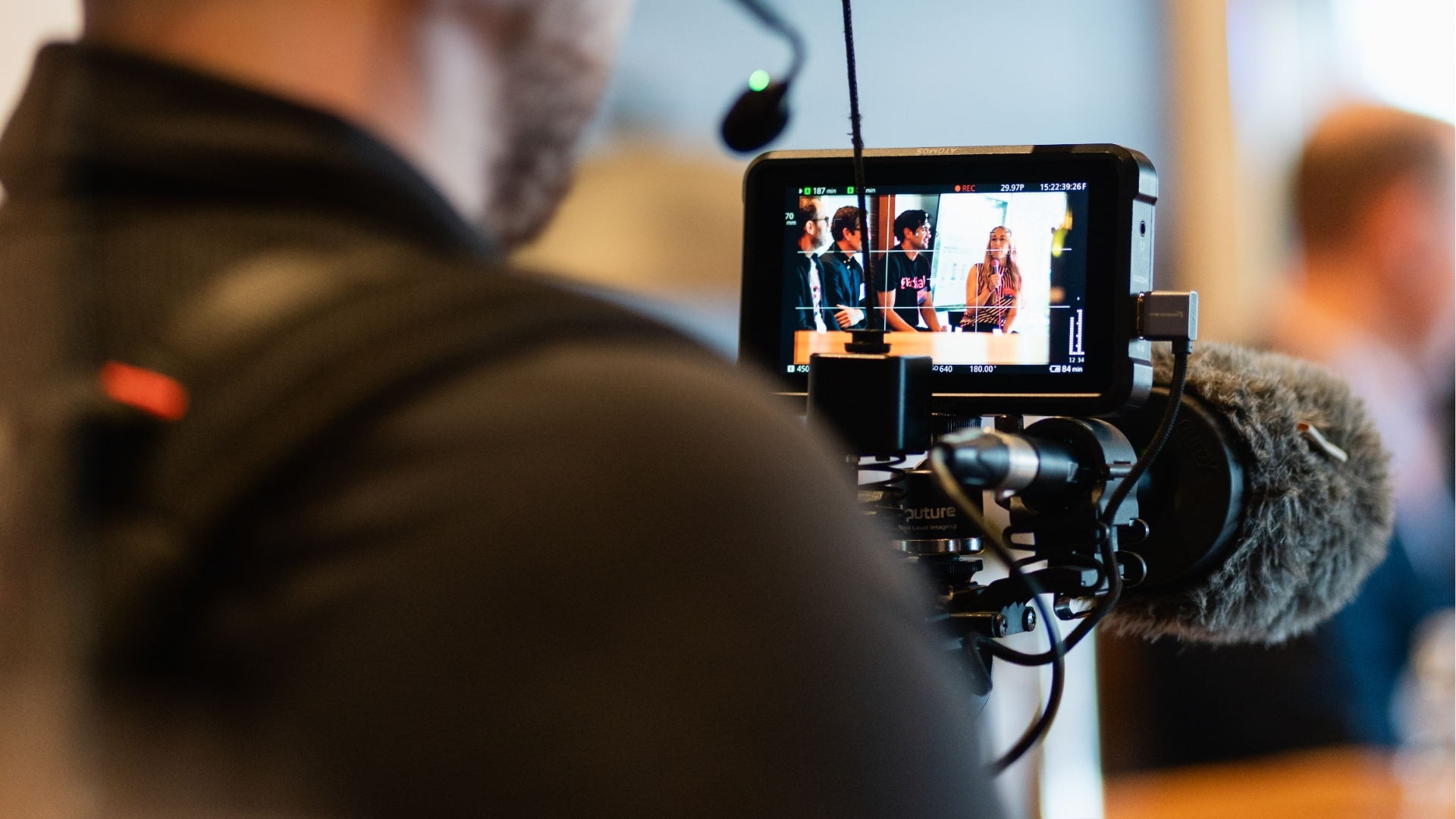 Camera monitor showing a group panel discussion with a woman speaking into a microphone.