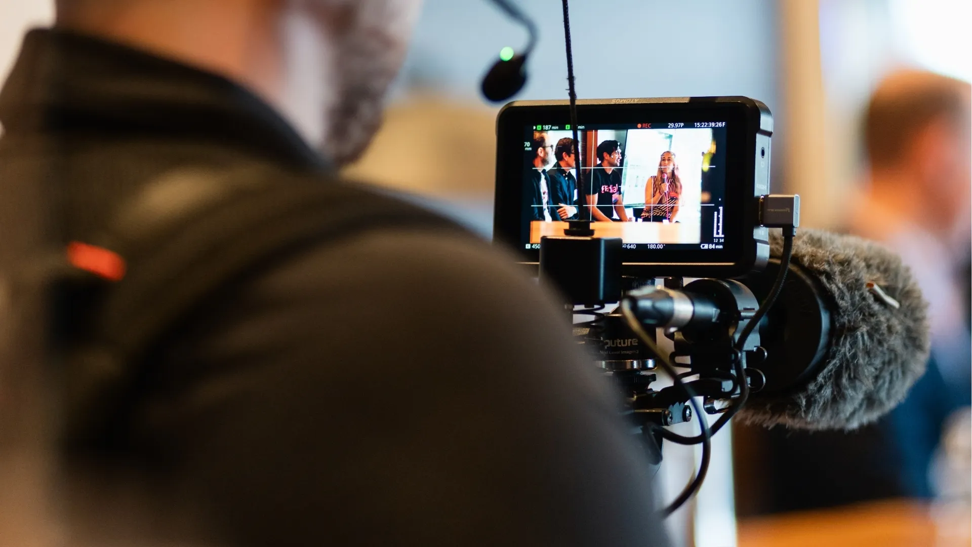 Camera monitor showing a group panel discussion with a woman speaking into a microphone.