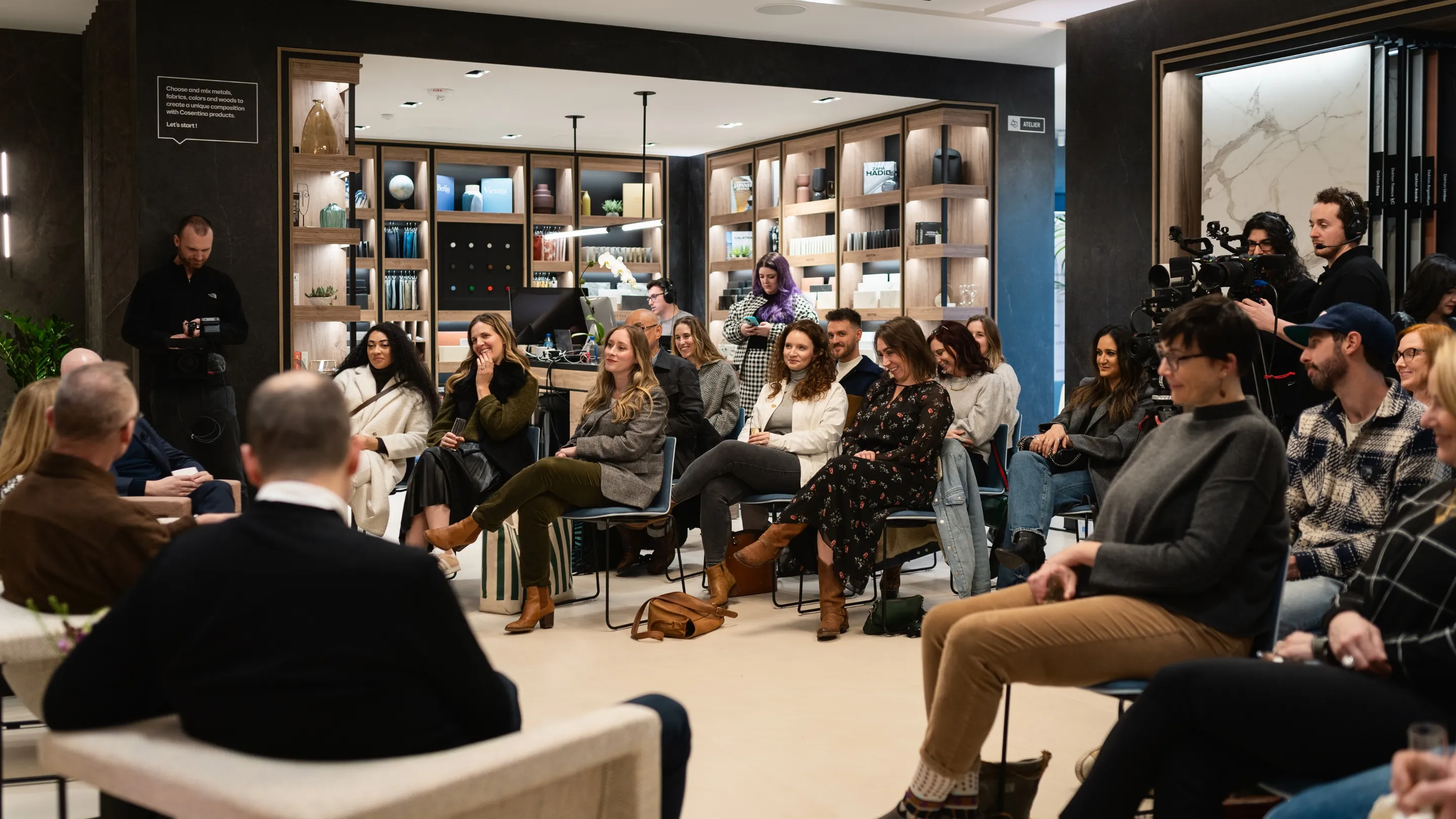 Group of people seated in a modern indoor setting, attentively listening and engaging in a discussion with two individuals facing them.