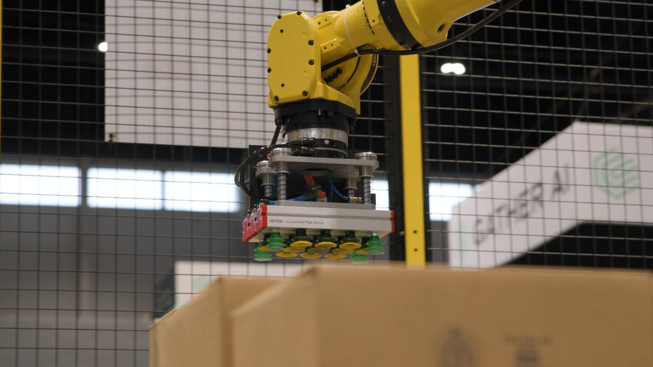 Yellow robotic arm with gripper attachment in industrial factory setting with grid ceiling