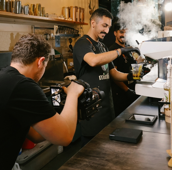 Barista making espresso drinks at coffee shop counter with steam and professional equipment.
