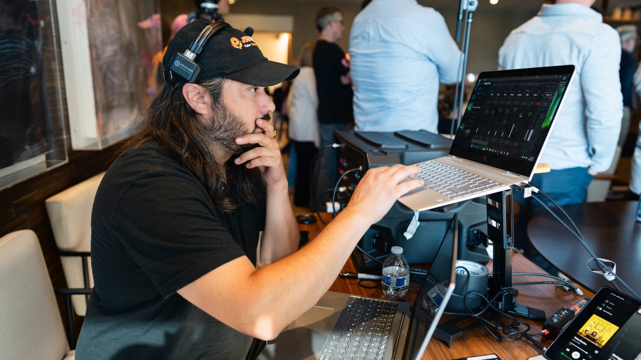 DJ with headphones and cap operating laptop at music event with crowd