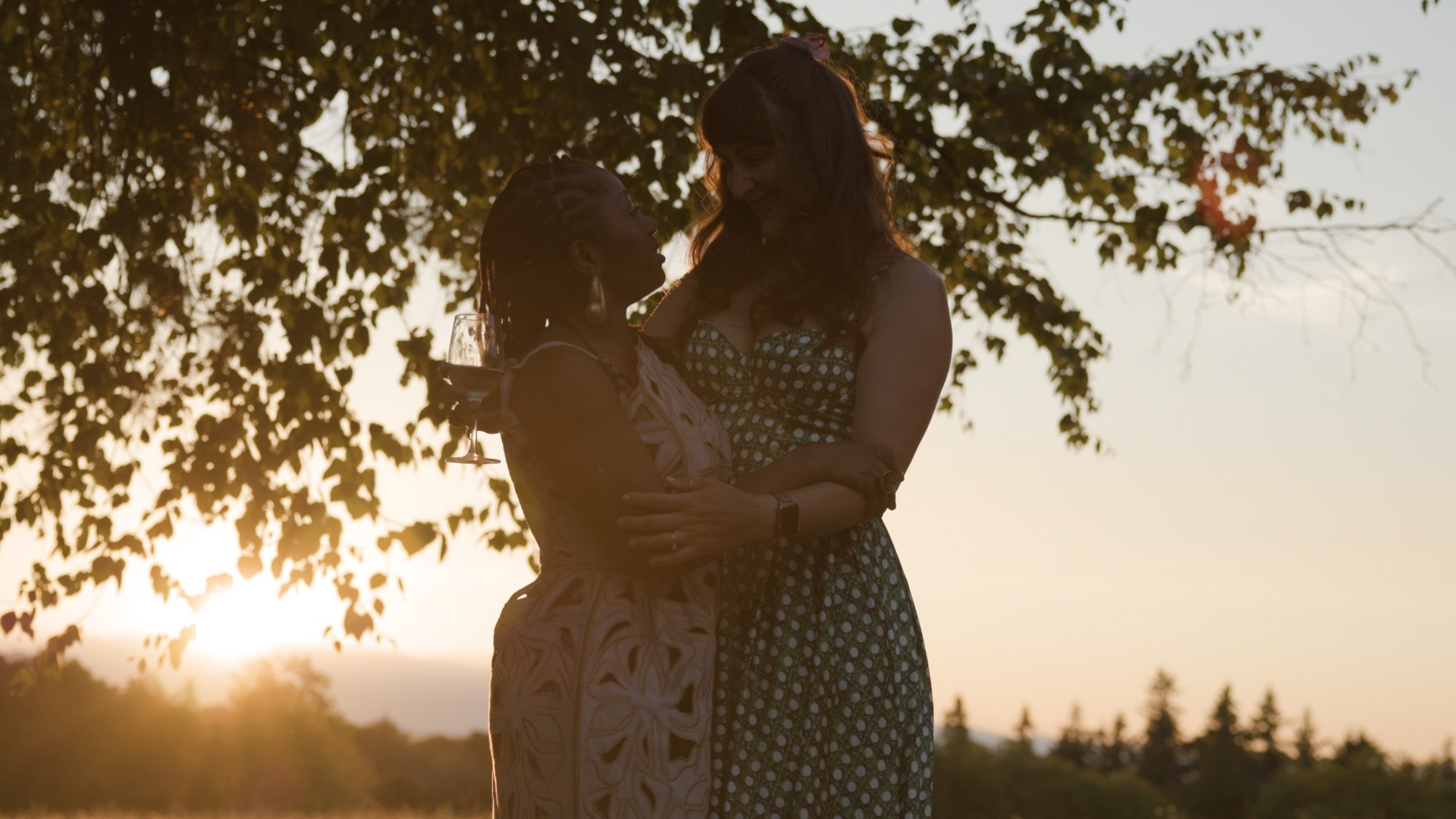Woman holding child under tree at sunset with forest in background