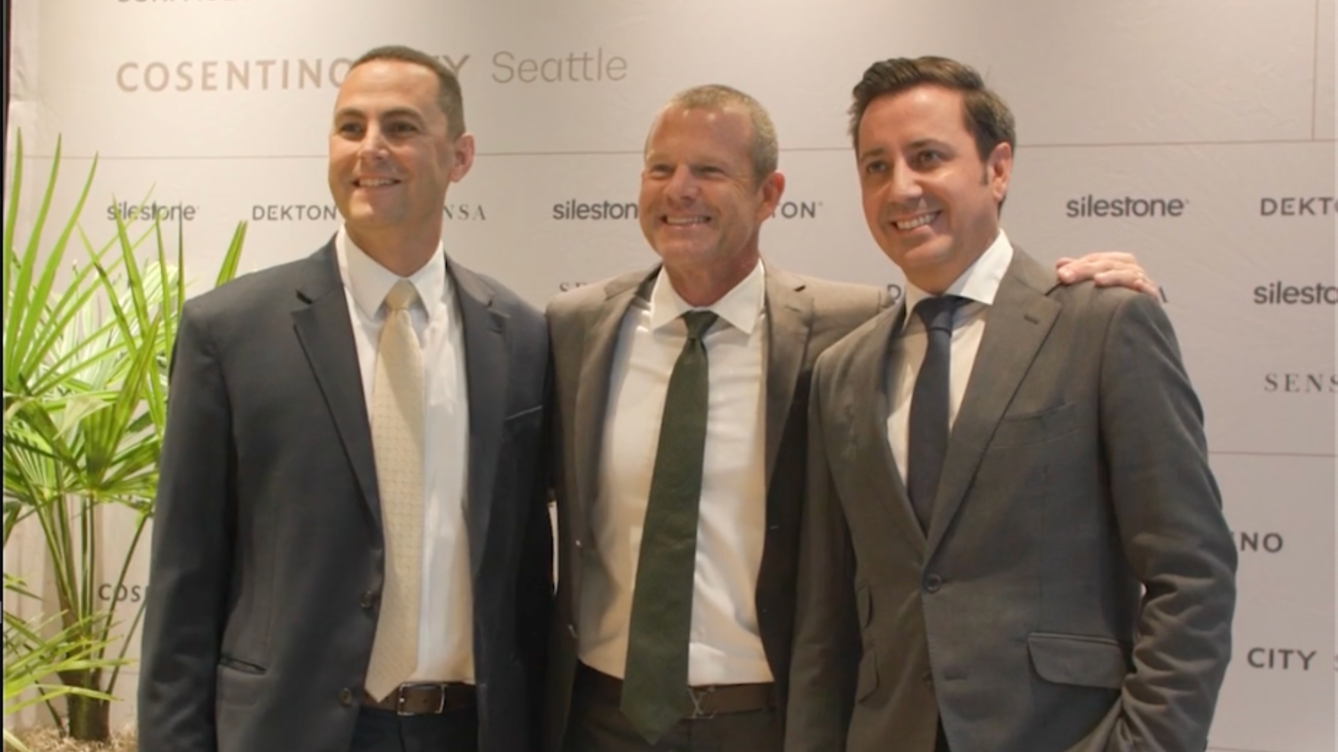 Three men in business suits posing together at a Seattle corporate event with backdrop logos