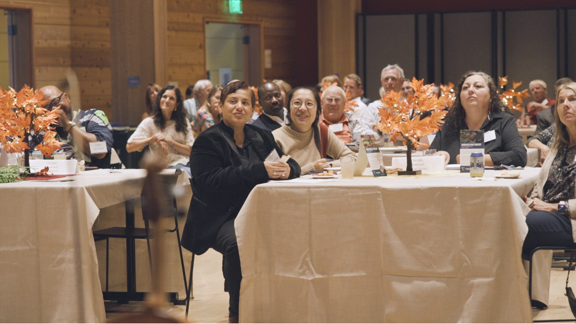 Conference attendees seated at tables with orange floral centerpieces in modern venue