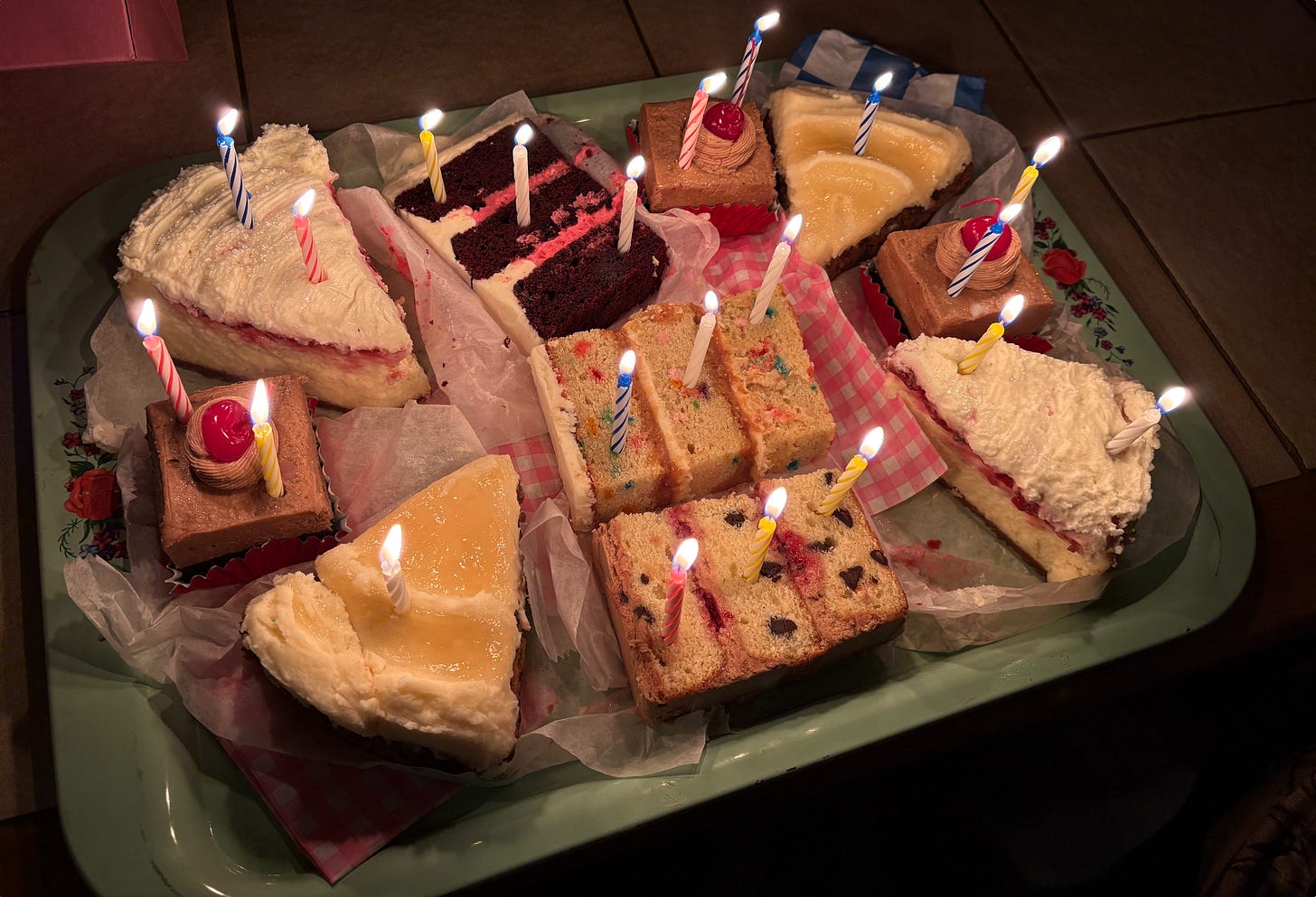 a spread of several slices of cake with lit arranged colorfully on a tray with lit birthday candles 