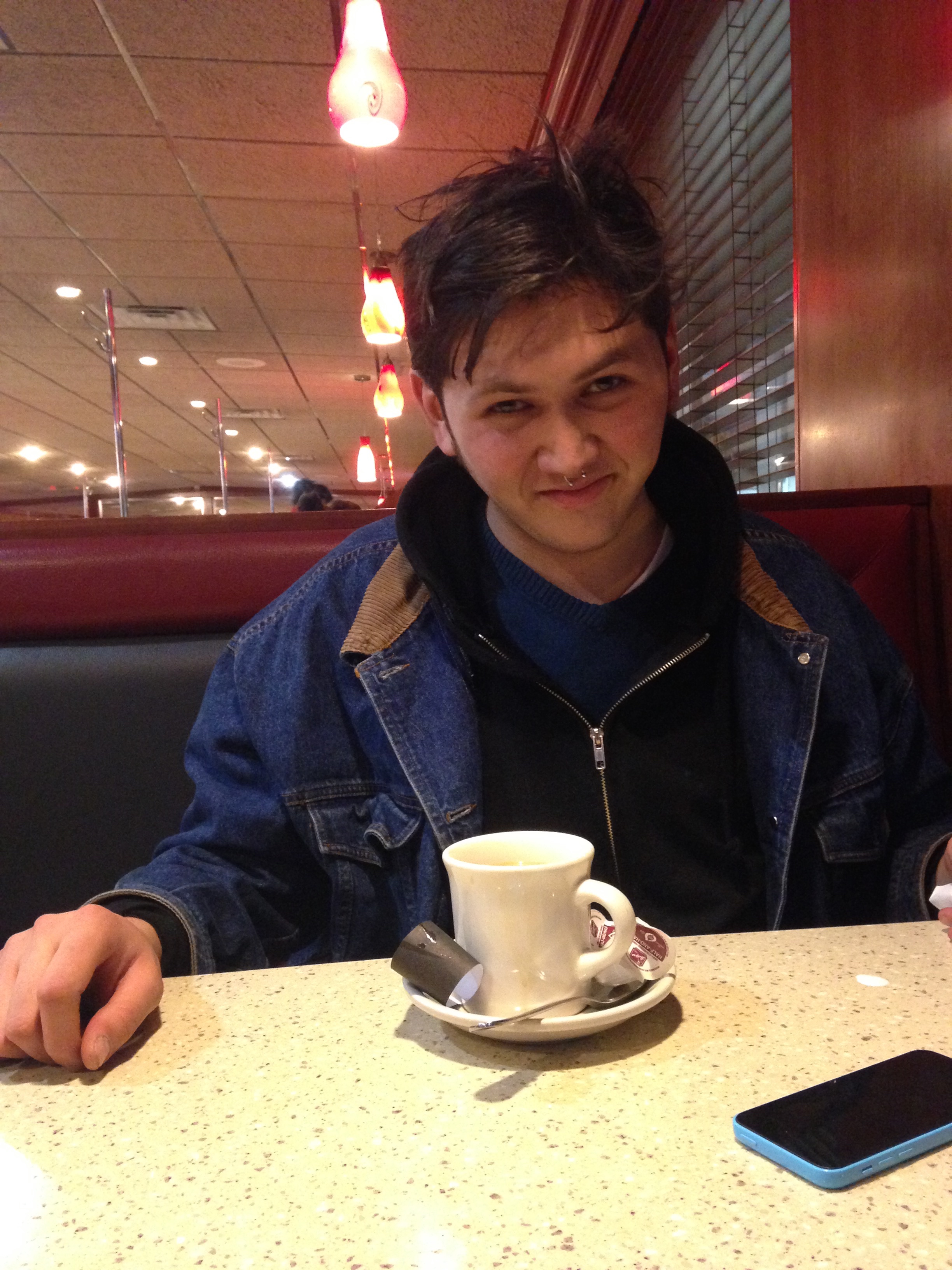 bml smirks at the camera and sits at a diner table with a mug and saucer in front of them