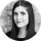 Black and white portrait of a woman with long straight hair smiling slightly, in front of a brick wall.