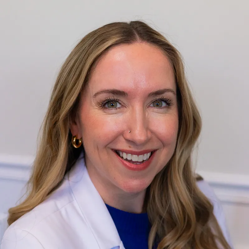 Smiling woman with curly hair, glasses, and a colorful flower crown filter.