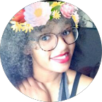 Smiling woman with curly hair, glasses, and a colorful flower crown filter.
