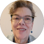 Portrait of a smiling middle-aged woman with short curly hair, glasses, and blue earrings.