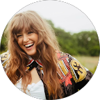 Smiling woman with long blonde hair wearing a colorful jacket outdoors.