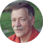 Portrait of a middle-aged man with gray hair, mustache, and wearing a red shirt, smiling outdoors.