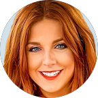 Close-up portrait of a smiling woman with long red hair and blue eyes.