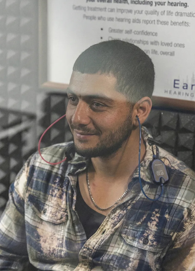 Man sitting in a soundproof room wearing earphones connected to a hearing test device.