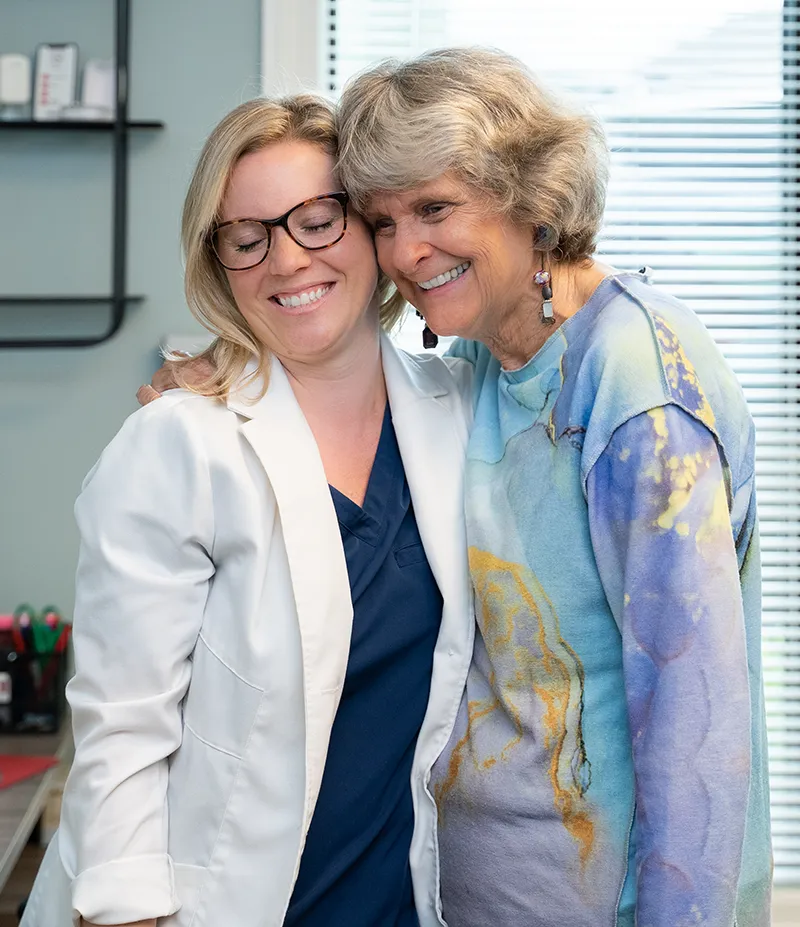 Dr Grome embracing an elderly female patient in a cheerful hug.