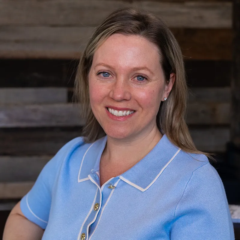Dr Grome with light brown hair wearing a light blue collared shirt against a wooden background.