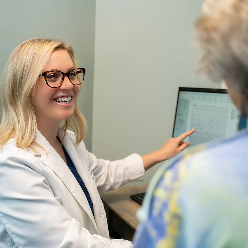 Dr Grome with glasses smiling and explaining data on a computer screen to a patient.