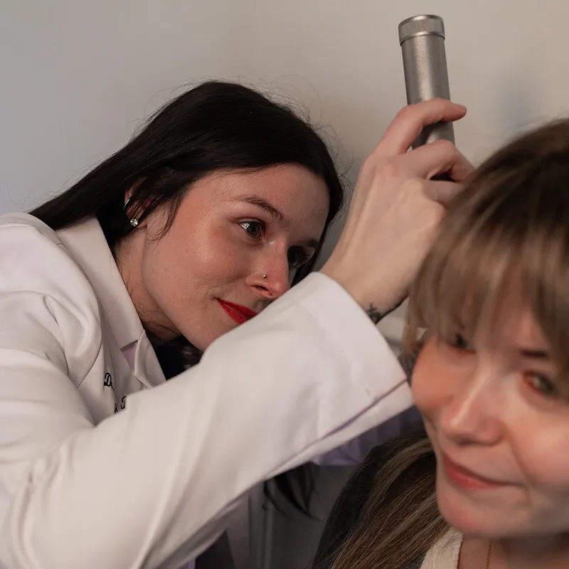 Audiologist using an otoscope to examine a patient's ear.