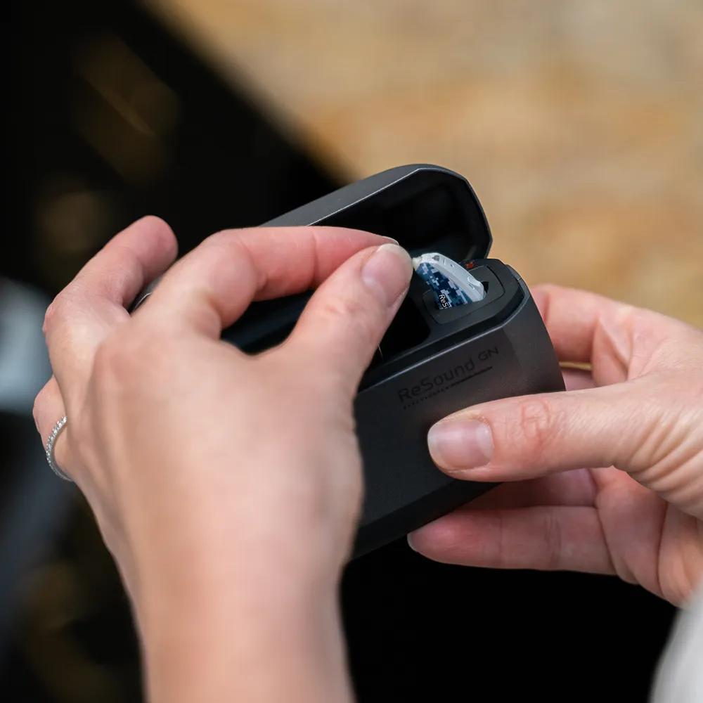 Person placing a blue-patterned ReSound hearing aid into a black charging case.