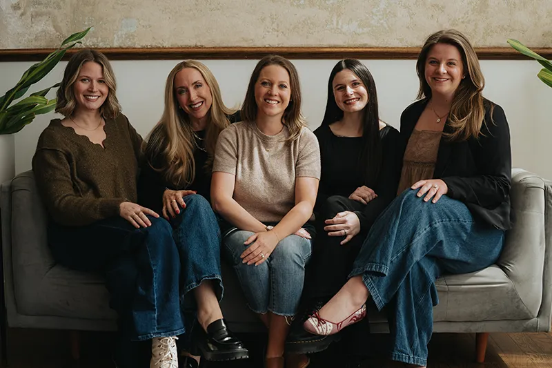 Ears4U staff standing indoors, three wearing white lab coats and one in a blue sweater, posing in front of a wooden wall.