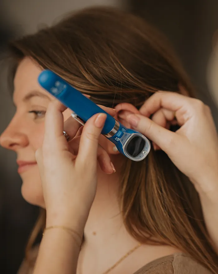Healthcare professional smiling while examining a smiling woman's scalp with a handheld device.
