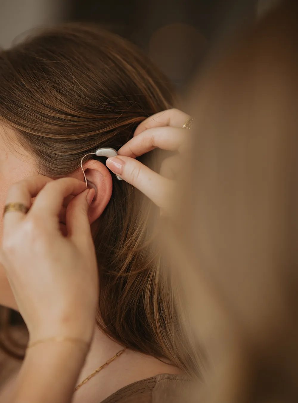 Close-up of hands holding a blue and white behind-the-ear hearing aid with an earmold.